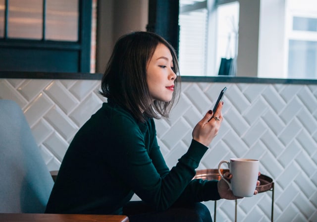 A woman looking at her smartphone and holding a coffee mug.